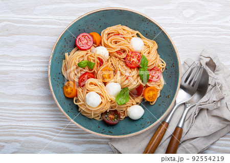spaghetti with mozzarella, colourful cherry tomatoes, fresh basil on ceramic plate spaghetti with mozzarella, colourful cherry tomatoes, fresh basil on ceramic plate 92554219