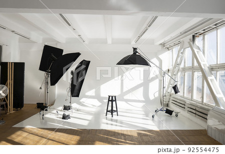 Professional lighting equipment, flashes, c-stands on a cyclorama in modern photo studio with a huge windows. Octabox, stripbox, softbox, buety plate and other stuff for photography. Professional lighting equipment, flashes, c-stands on a cyclorama in modern photo studio with a huge windows. Octabox, stripbox, softbox, buety plate and other stuff for photography. 92554475