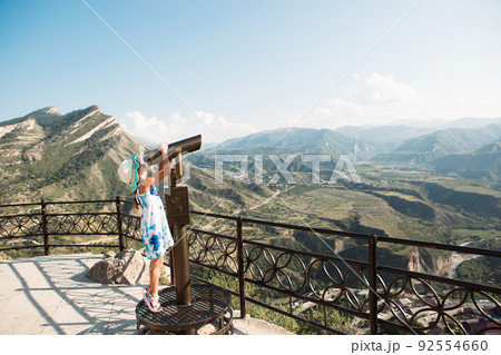 Tourist girl looks through binoculars from a height on the observation deck at mountain landscape. Sightseeing tour. Dagestan, Caucasus Mountains Tourist girl looks through binoculars from a height on the observation deck at mountain landscape. Sightseeing tour. Dagestan, Caucasus Mountains 92554660