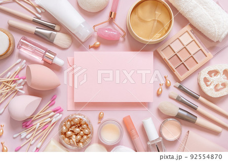 Paper card between skin care and decorative cosmetics on pink, top view, mockup 92554870