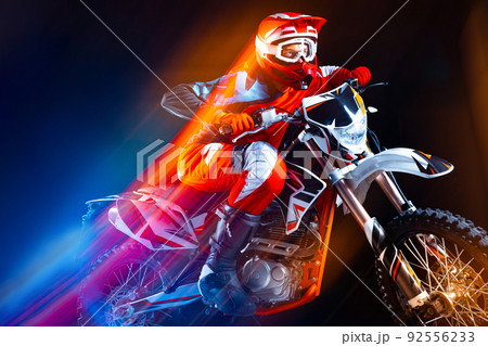 Portrait of young man, biker riding motorbike isolated over black background in neon with mixed lights. Speed development. Portrait of young man, biker riding motorbike isolated over black background in neon with mixed lights. Speed development. 92556233