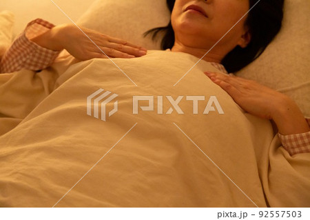 パジャマを着て布団で寝るミドル女性 92557503