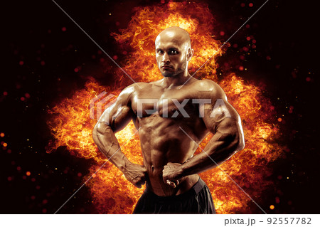 Brutal strong athletic Bodybuilder posing. Fire and spark explosion in the background. 92557782