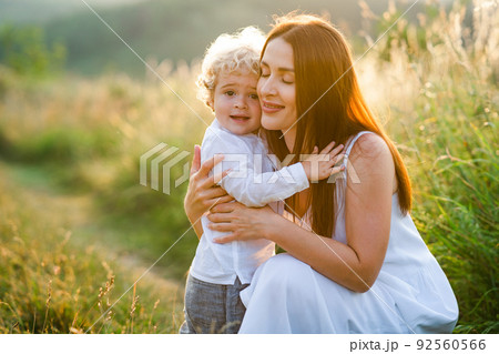 Loving mother hugs her son while walking in a picturesque field. 92560566