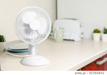 A small fan on the kitchen table. The concept of cooling and ventilation of the house. A small fan on the kitchen table. The concept of cooling and ventilation of the house. 92560842