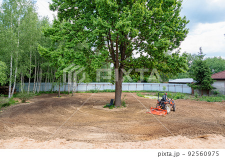 A man on a mini-excavator levels a piece of land, loosens the soil. 92560975