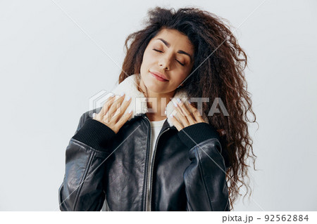 Calm Happy Curly Pensive Latin Woman Enjoying Soft Fur Warm Black Leather Jacket Collar Posing Isolated Closing Eyes At White Studio Wall Background. Fashion Huge Sale New Collection Concept 92562884