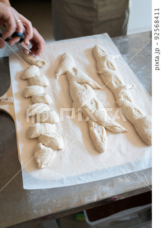 The process of making French traditional bread. Baguettes ear, notching the dough. Vertical photo. 92568411