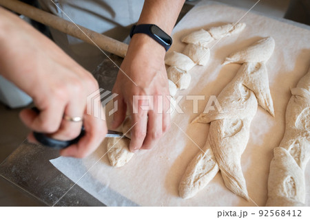 The process of making French traditional bread. Baguettes ear, notching the dough. Front view. The process of making French traditional bread. Baguettes ear, notching the dough. Front view. 92568412