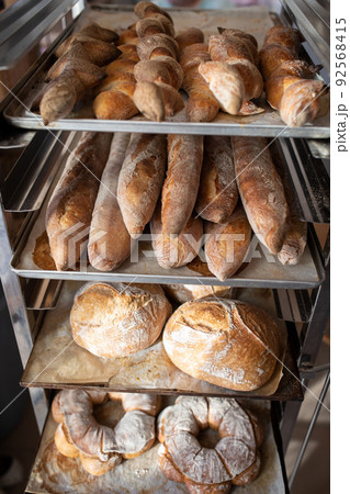 Finished French bread in the bakery on the racks. Baguettes, rustic bread, crown of kings Bordeaux. Vertical photo. Finished French bread in the bakery on the racks. Baguettes, rustic bread, crown of kings Bordeaux. Vertical photo. 92568415