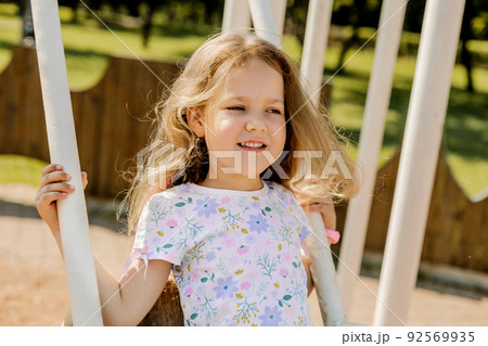 Portrait of a beautiful girl swinging on a swing on a summer day. Childhood, recreation, summer time Portrait of a beautiful girl swinging on a swing on a summer day. Childhood, recreation, summer time 92569935