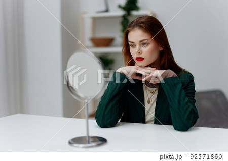 A red-haired beauty in a green jacket is going to a party in front of a mirror at home 92571860