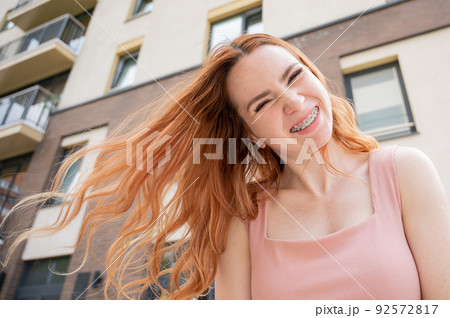 Beautiful young red-haired woman with braces on her teeth smiling in the summer outdoors Beautiful young red-haired woman with braces on her teeth smiling in the summer outdoors 92572817