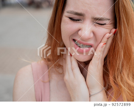 Young red-haired woman with braces suffering from pain. Young red-haired woman with braces suffering from pain. 92572899