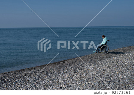 Pacified caucasian woman in a wheelchair on the seashore. Pacified caucasian woman in a wheelchair on the seashore. 92573261