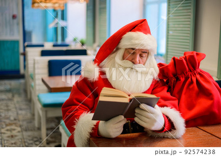 Santa Claus is sitting in a cafe and reading a book Santa Claus is sitting in a cafe and reading a book 92574238