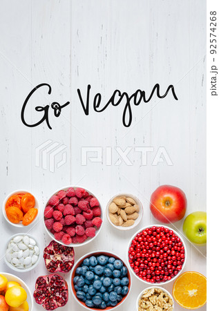 Fresh berries, fruits, nuts on a white wooden background. The concept of healthy eating. Food contains vitamins and trace elements. Go vegan - handwritten inscription. 92574268