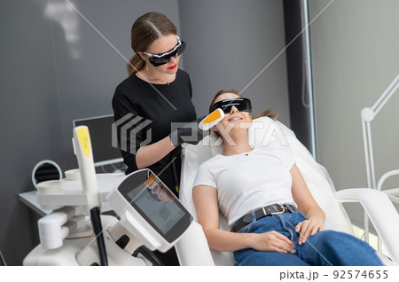 A woman on a couch in goggles undergoing a photorejuvenation procedure. Hardware cosmetology.  92574655