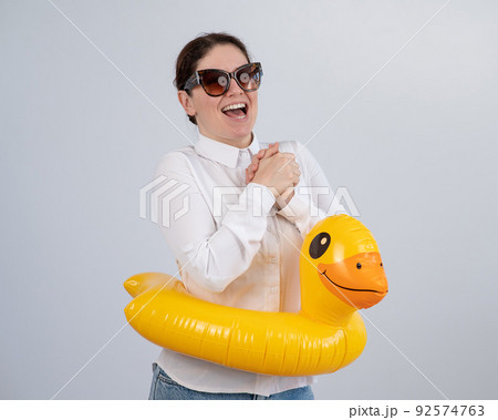 Caucasian woman in a white shirt dreaming of a vacation and wearing sunglasses and an inflatable duck. Caucasian woman in a white shirt dreaming of a vacation and wearing sunglasses and an inflatable duck. 92574763