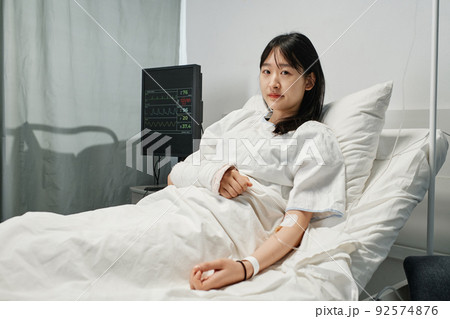 Horizontal medium shot of young Asian woman with arm broken after accident lying on hospital bed in emergency room getting IV therapy Horizontal medium shot of young Asian woman with arm broken after accident lying on hospital bed in emergency room getting IV therapy 92574876