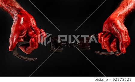 A man with bloody hands holds iron handcuffs. 92575525