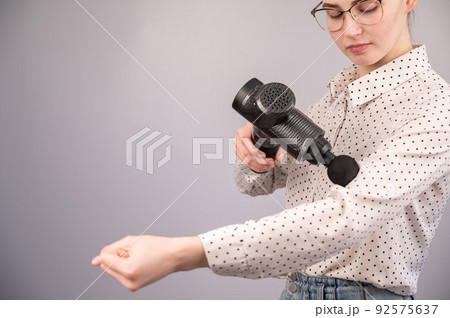 Caucasian business woman massaging her biceps with a percussion massager. Caucasian business woman massaging her biceps with a percussion massager. 92575637