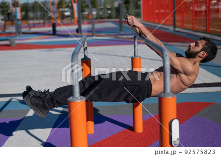 Shirtless man doing horizontal balance on parallel bars at sports ground.  92575823