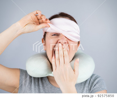 Caucasian woman yawns with travel pillow and sleep mask on white background. Caucasian woman yawns with travel pillow and sleep mask on white background. 92575850