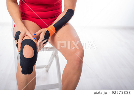 The athlete puts a medical tape on his knee. alternative treatment for joint and tendon injuries. Physiotherapy of chronic inflammation of the joints of the female leg. 92575858