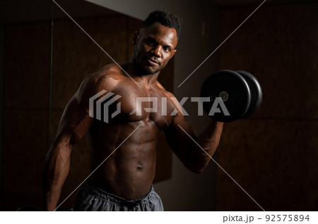 Attractive african american man doing biceps exercise with dumbbells.  92575894