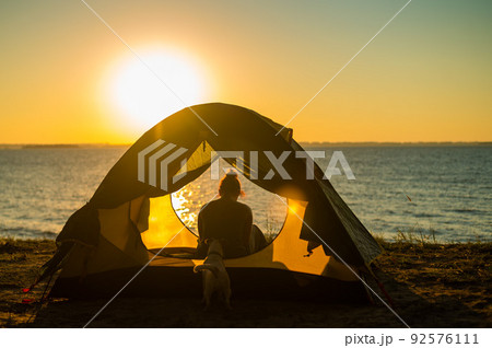 Woman and dog in a tourist tent at sunset. Camping with a pet Woman and dog in a tourist tent at sunset. Camping with a pet 92576111