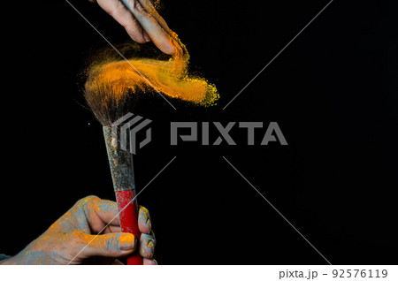 Woman shaking off orange powder from a brush on a black background. Woman shaking off orange powder from a brush on a black background. 92576119