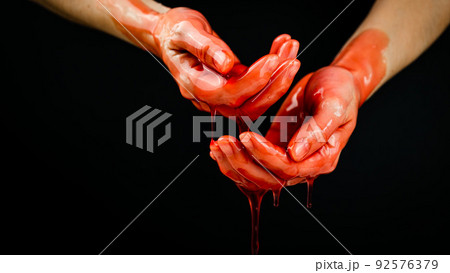 Women's hands in a viscous red liquid similar to blood. 92576379