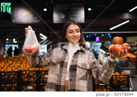 Eco friendly woman buys apples in the supermarket. Female grocery shopper opposes the use of plastic bags 92579094