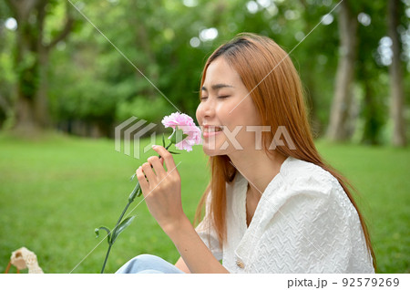 Beautiful Asian female in the garden, admiring pink flower in her hand, smelling the flower. 92579269