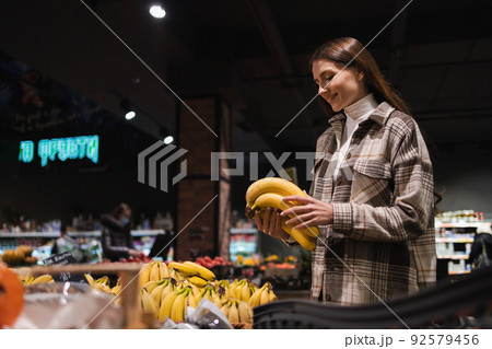 Young cheerful woman with bananas in hands in a supermarket Young cheerful woman with bananas in hands in a supermarket 92579456