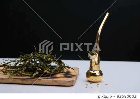 Close-up of cannabis leaves on a wooden board and smoke coming out of a pipe on a black background. Cannabis legalisation. 92580002