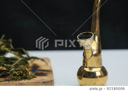 Close-up of cannabis leaves on a wooden board and smoke coming out of a pipe on a black background. Cannabis legalisation. Close-up of cannabis leaves on a wooden board and smoke coming out of a pipe on a black background. Cannabis legalisation. 92580006