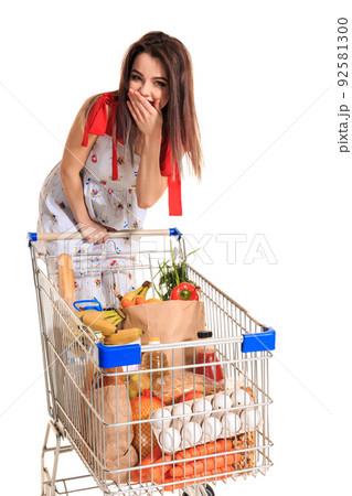 A young female pushing a shopping cart full with groceries isolated on white background. A woman laughs and closes her mouth with her palm 92581300