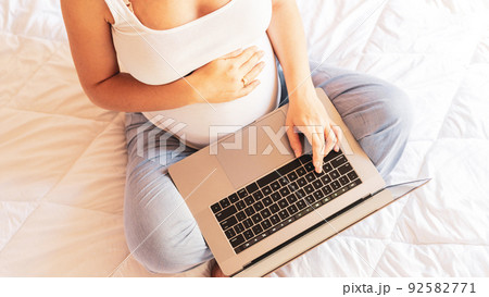 Pregnancy computer app. Pregnant woman holding digital laptop. Mobile pregnancy online maternity notebook application. Concept maternity, pregnancy, childbirth. 92582771