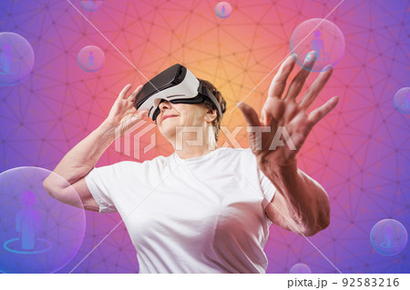 Metaverse and virtual reality. Smiling senior woman in VR glasses touching digital sphere with symbol of human. Purple background with neon grid. Concept of retiree, social media and cyberspace 92583216