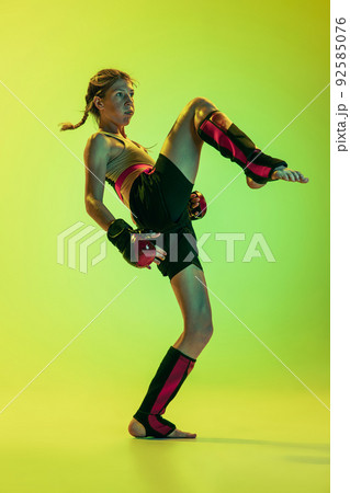 Dynamic portrait of athletic girl, MMA fighter training isolated on gradient yellow-green background in neon. Concept of sport, energy, combat sports 92585076