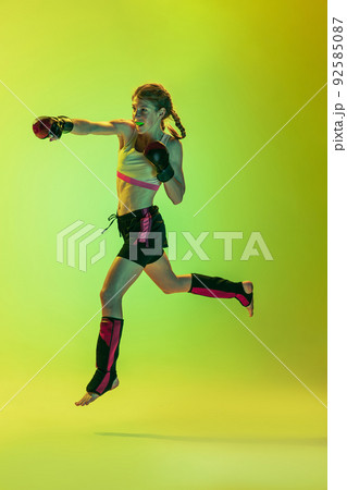 Dynamic portrait of athletic girl, MMA fighter training isolated on gradient yellow-green background in neon. Concept of sport, energy, combat sports Dynamic portrait of athletic girl, MMA fighter training isolated on gradient yellow-green background in neon. Concept of sport, energy, combat sports 92585087