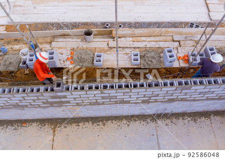 The construction site is being worked on by workers who are laying masonry blocks and cinder concrete blocks on scaffolding The construction site is being worked on by workers who are laying masonry blocks and cinder concrete blocks on scaffolding 92586048