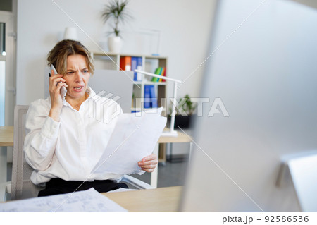 Business woman with a surprised face talking on the phone while looking at documents 92586536