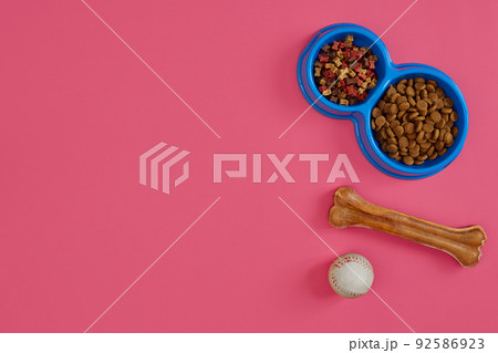 Dry pet food in bowl with a ball and dog bone on pink background top view Dry pet food in bowl with a ball and dog bone on pink background top view 92586923