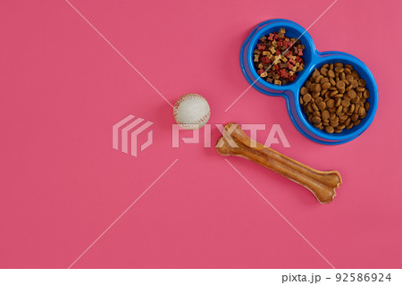 Dry pet food in bowl with a ball and dog bone on pink background top view Dry pet food in bowl with a ball and dog bone on pink background top view 92586924
