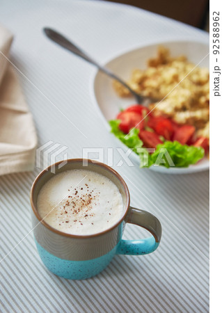 Cappuccino coffee in cup and plate with scrambled eggs and tomatoes. Breakfast on the table Cappuccino coffee in cup and plate with scrambled eggs and tomatoes. Breakfast on the table 92588962