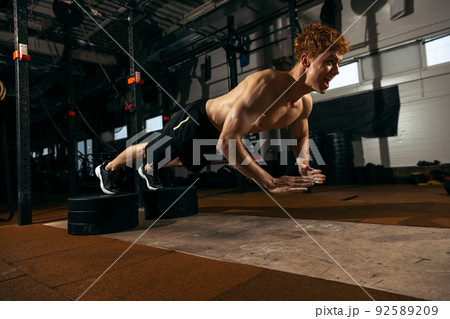 Portrait of young sportive man with muscular body training, doing push-ups exercises isolated over geym background. In the air Portrait of young sportive man with muscular body training, doing push-ups exercises isolated over geym background. In the air 92589209
