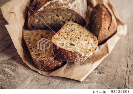 Brown fresh bread with seeds are cut into pieces on old wood background. Top view, copy space 92589803